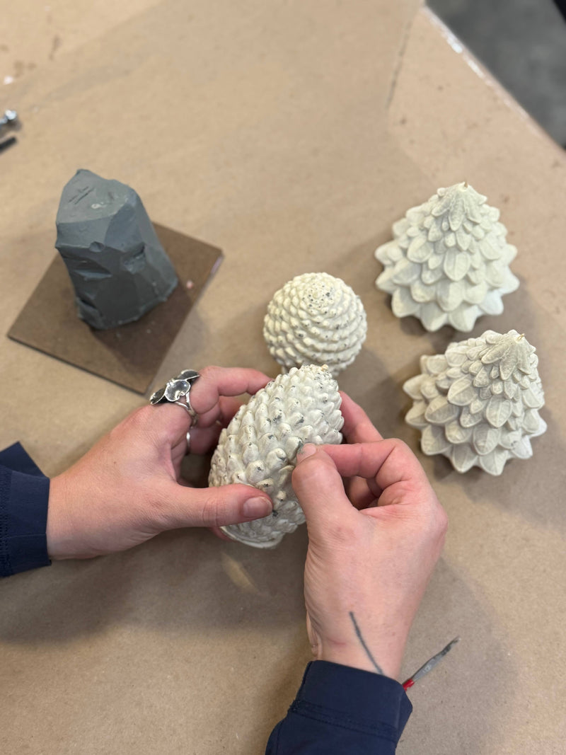 Mo&Co Home Exclusive: Sculpted Beeswax Pine Cones being hand-refined in a studio, showcasing detailed craftsmanship and artistry for elegant holiday decor. Available in two sizes.