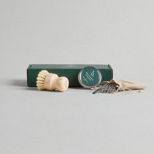 Smithey Cleaning & Care Kit with a wooden brush, seasoning tin, burlap pouch, and chain-mail scrubber, designed for maintaining cast iron cookware.