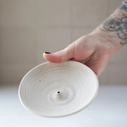Hand holding a Gravesco Pottery - Incense Burner, a minimalist white ceramic dish with a central holder for incense sticks, perfect for catching ash.