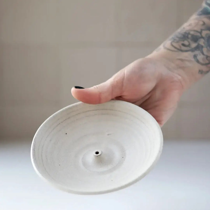 Hand holding a Gravesco Pottery - Incense Burner, a minimalist white ceramic dish with a central holder for incense sticks, perfect for catching ash.