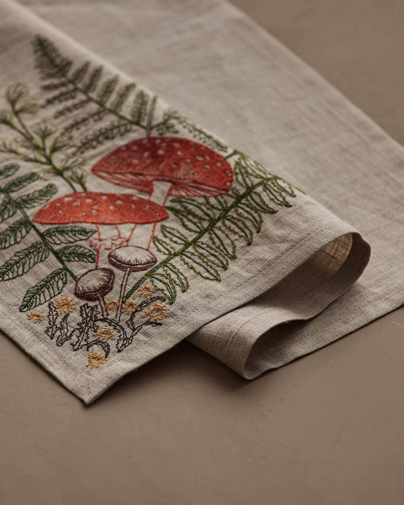 Coral & Tusk - Mushrooms and Ferns Bouquet Dinner Napkin features embroidered ferns and mushrooms on natural linen, ideal for a whimsical table setting. Measures 20 × 20.