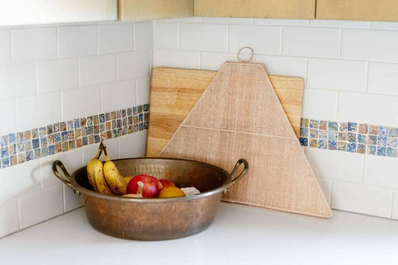 NEEPA HUT | Collapsible Woven Food Tent - Rose Pink protects a bowl of fruit on a kitchen counter, showcasing its unique pentagon shape and craftsmanship.