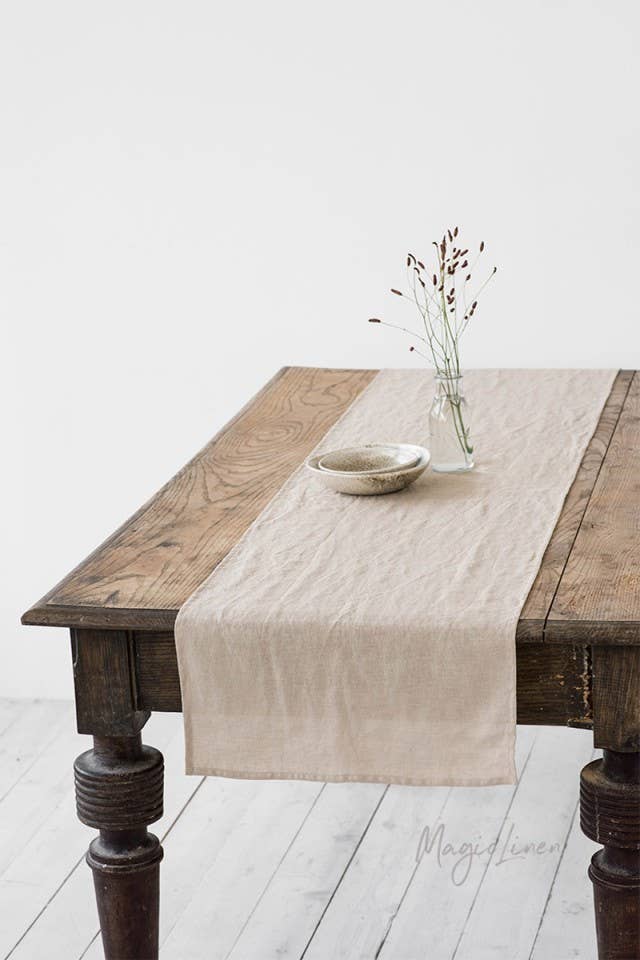Linen table runner displayed on a table with a vase and bowl, showcasing its soft texture and decorative appeal.