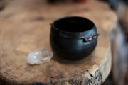 Gravesco Pottery - Black Cauldron Bowl, handcrafted, matte black, palm-sized with a quartz crystal, on a wooden surface, embodying artisanal charm for Halloween.