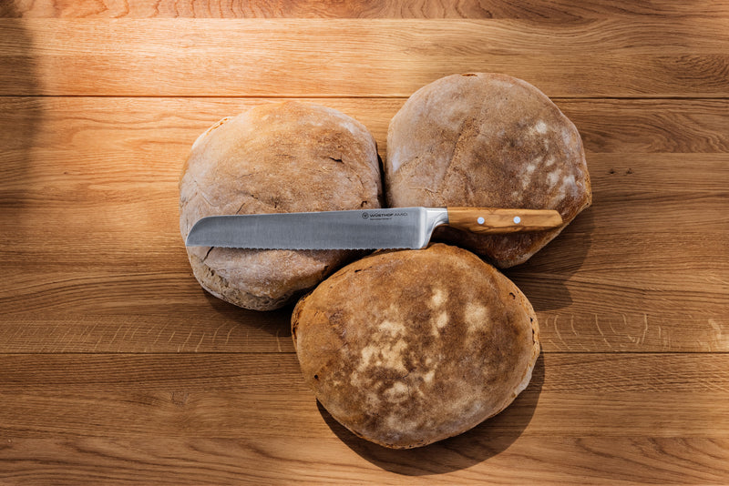 Wüsthof | Amici 9 Double Serrated Bread Knife beside a sliced loaf, showcasing its precision cutting on a wooden surface.