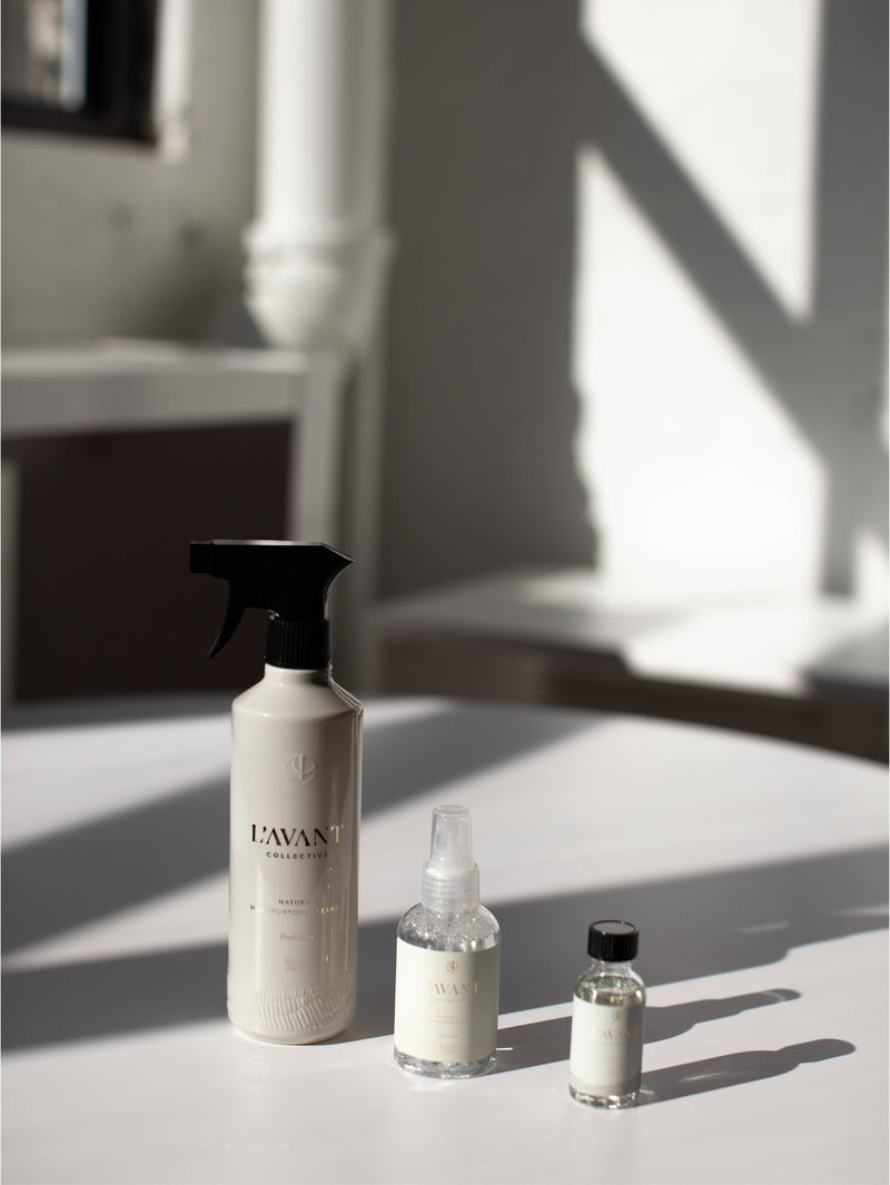 L'AVANT Collective - Fresh Linen Multipurpose Cleaner Refill in eco-luxe glass bottles, displayed with a spray bottle on a table.