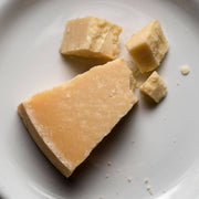 Nicola's Marketplace - Parmigiano Reggiano DOP Mitica® 36 months: 7 Ounces, crumbly pieces on a white plate, showcasing authentic aged Italian cheese from Emilia Romagna.