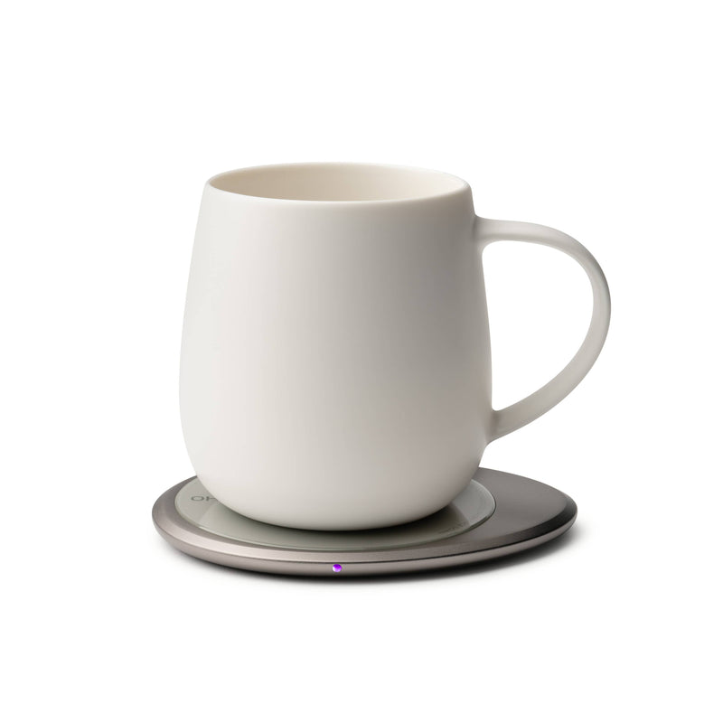 OHOM - Ui 3 Self-heating Mug Set: Jasmine White shown on an electric coaster, keeping beverages warm, with wireless phone charging capability.