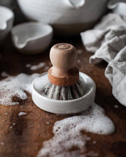Farmhouse Pottery - Laurel Pot Brush Set: A wooden-handled scrub brush with natural bristles in a soap-filled ceramic dish, perfect for efficient cleaning in a kitchen setting.