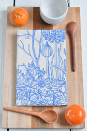 Hearth and Harrow - Kitchen Herbs Tea Towel in Blue-violet, displayed with oranges and a wooden handle, highlighting its utility and elegance for kitchen use.