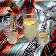 Zwiesel Fortessa | Veranda Double Old Fashioned Clear 14oz Tumbler on a picnic setup, with a glass pitcher of lemonade and a vibrant woven blanket.