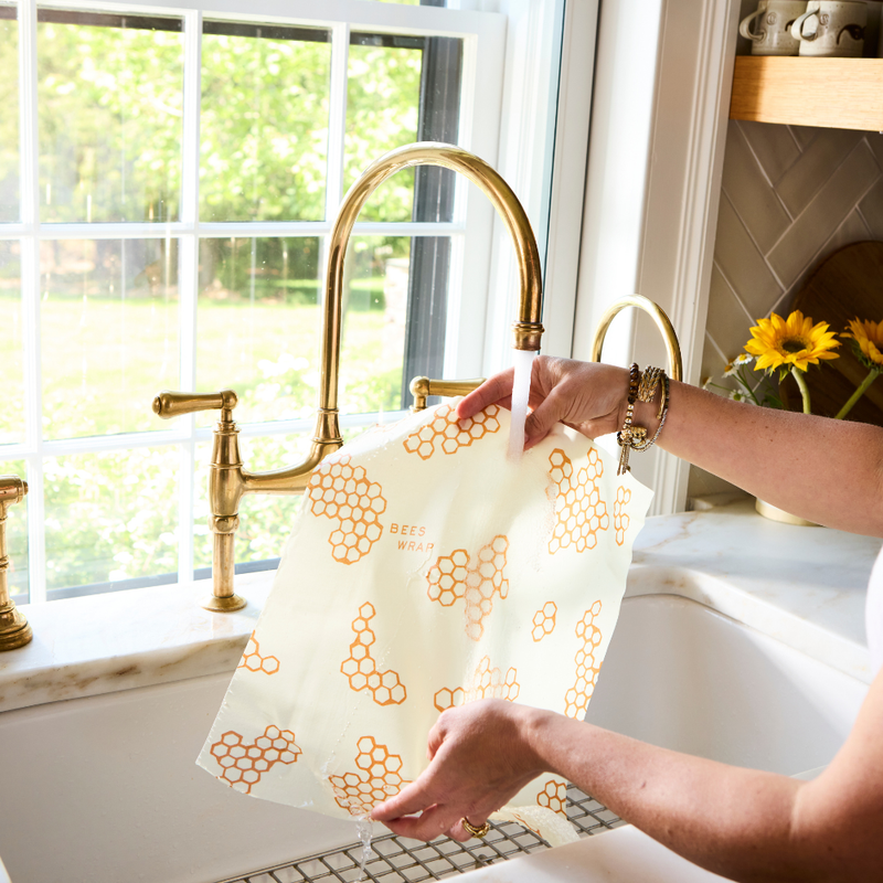 Bee's Wrap - Assorted 5 Pack - Honeycomb held by a woman near a kitchen sink, illustrating its use for storing kitchen items sustainably.