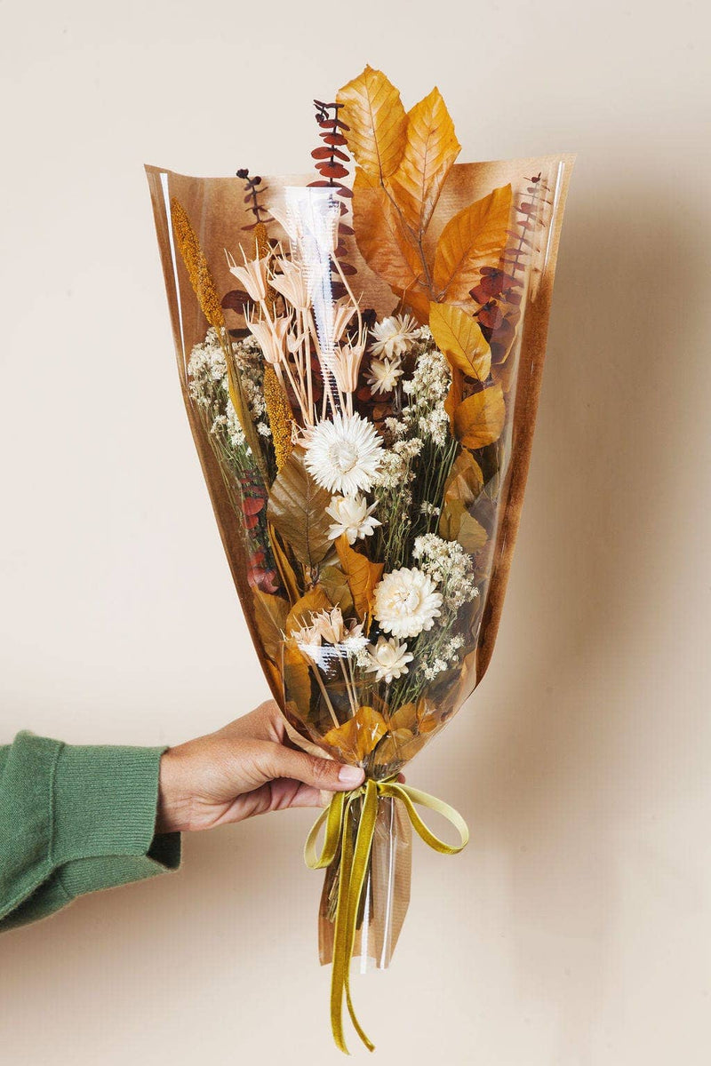 Idlewild Floral Co. - Golden Fall Market Bouquet, a hand-held dried floral arrangement featuring cream-white blooms and golden foliage, wrapped in cellophane and craft paper with a velvet ribbon.