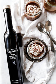 Kosterina - Dark Chocolate Balsamic Vinegar (375ml) bottle next to a glass jar of chocolate pudding with whipped cream.