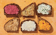 Six slices of hearty, seeded bread with diverse spreads, showcasing recipes from By Heart by Penguin Random House LLC, available at Athens Cooks.