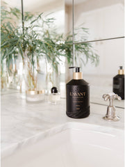 L'AVANT Collective Fresh Linen Hand Soap in a matte black glass bottle with a gold lid, positioned on a white counter in a bathroom setting.
