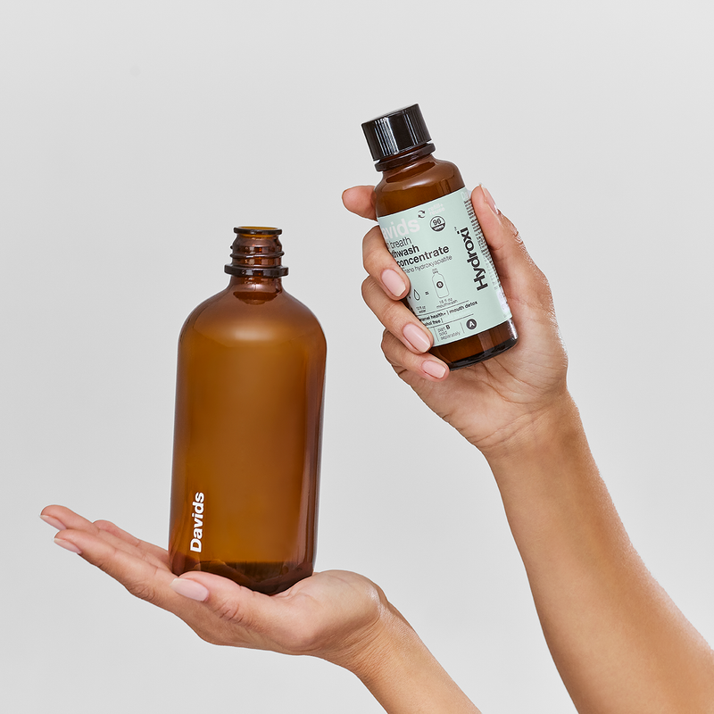 Hands holding Davids Hydroxi™ fresh breath mouthwash: one reusable 16oz bottle and one 4oz refill concentrate, featuring natural mint blend for oral health.