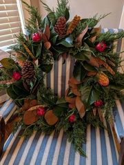 Lucknow Southern and Company - Southern Christmas Wreath features live evergreens and dried foliage, accented with magnolia leaves, pine cones, and red fruits on a chair.