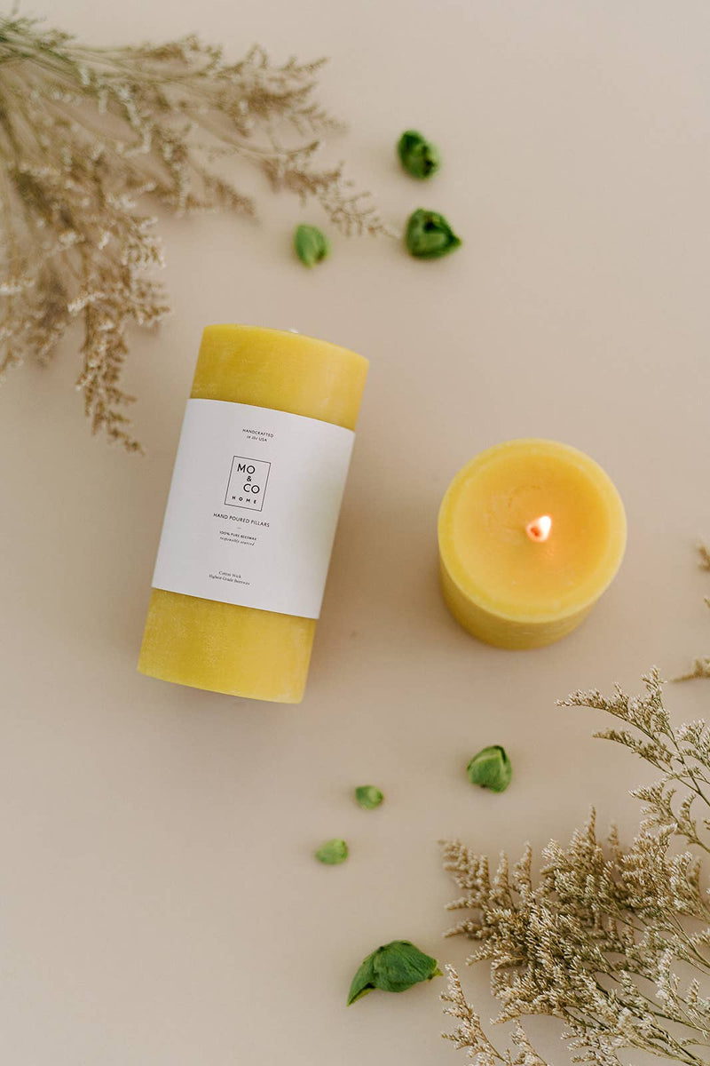 Mo&Co Home - 100% Beeswax Pillar Candles | Natural Gold: 3x6 Inch. Hand-poured, eco-friendly, displayed next to leafy greens, ideal for enhancing home and special occasions.