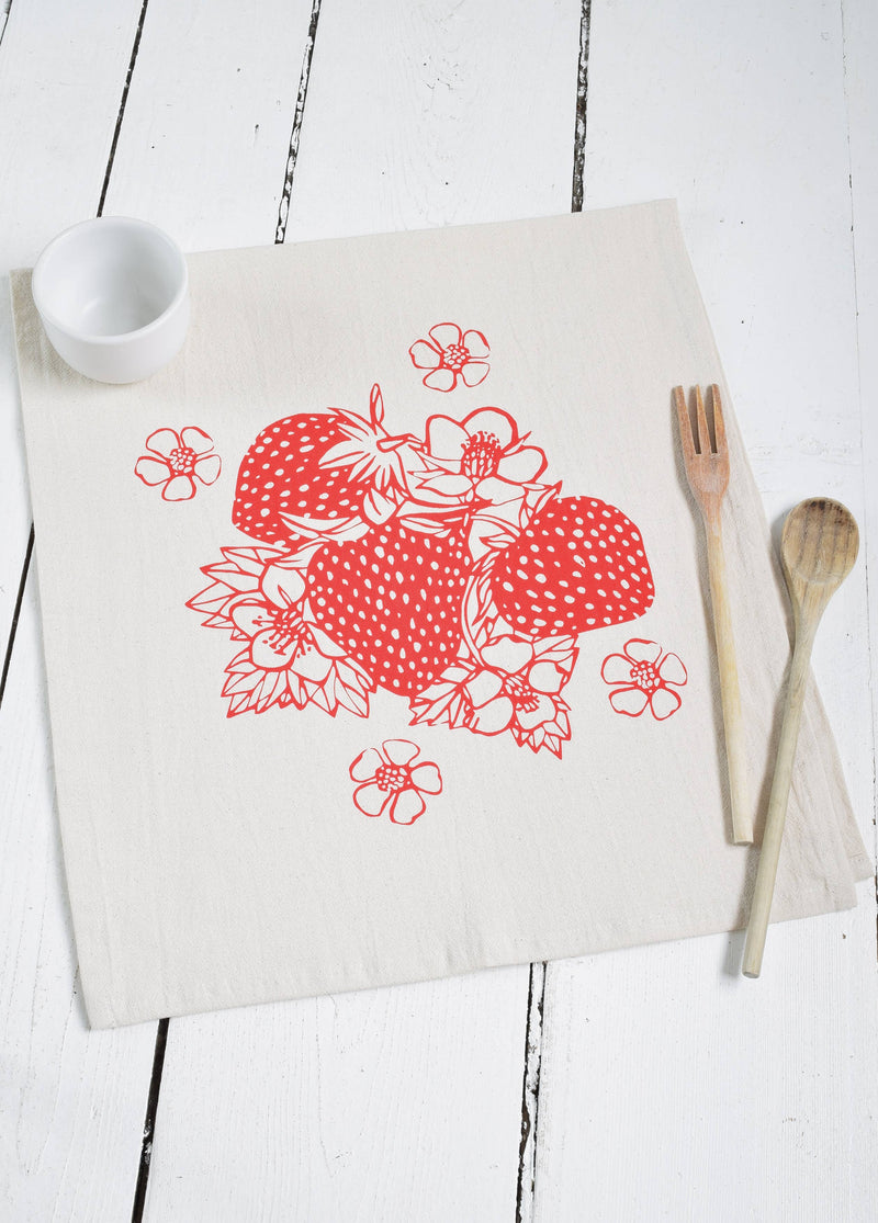 Hearth and Harrow - Strawberry Tea Towel features a red fruit print on organic cotton, ideal for kitchen use, displayed with a spoon and fork on a napkin.