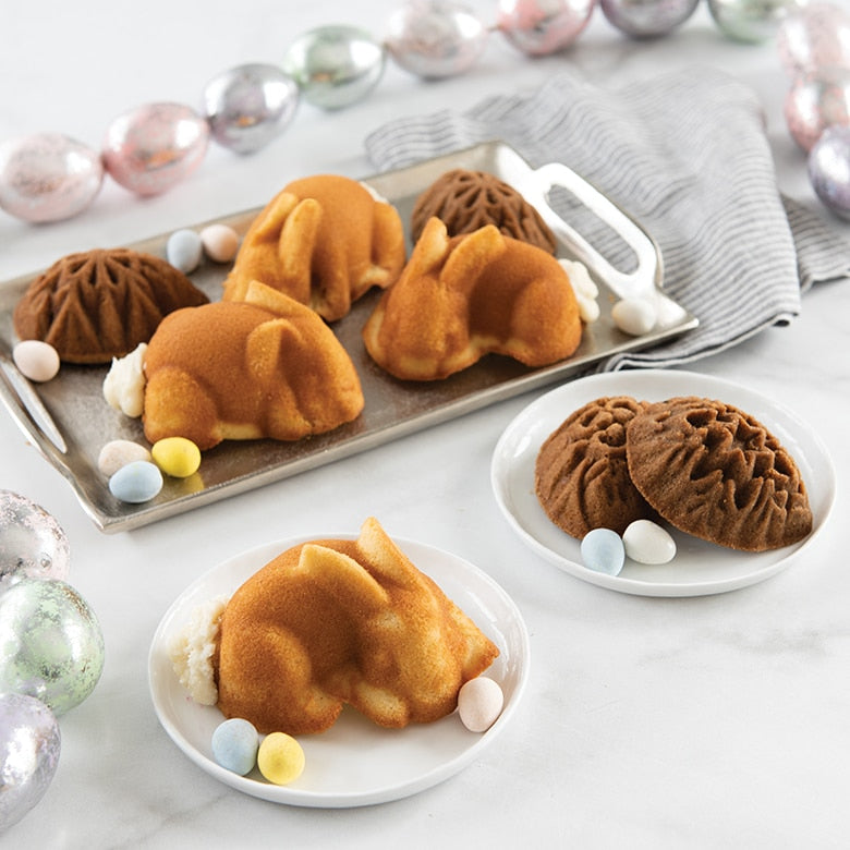 Nordic Ware | Baby Bunny Cake Pan displayed with bundt cakes and candies, showcasing its detailed bunny shape and nonstick surface for easy baking and release.