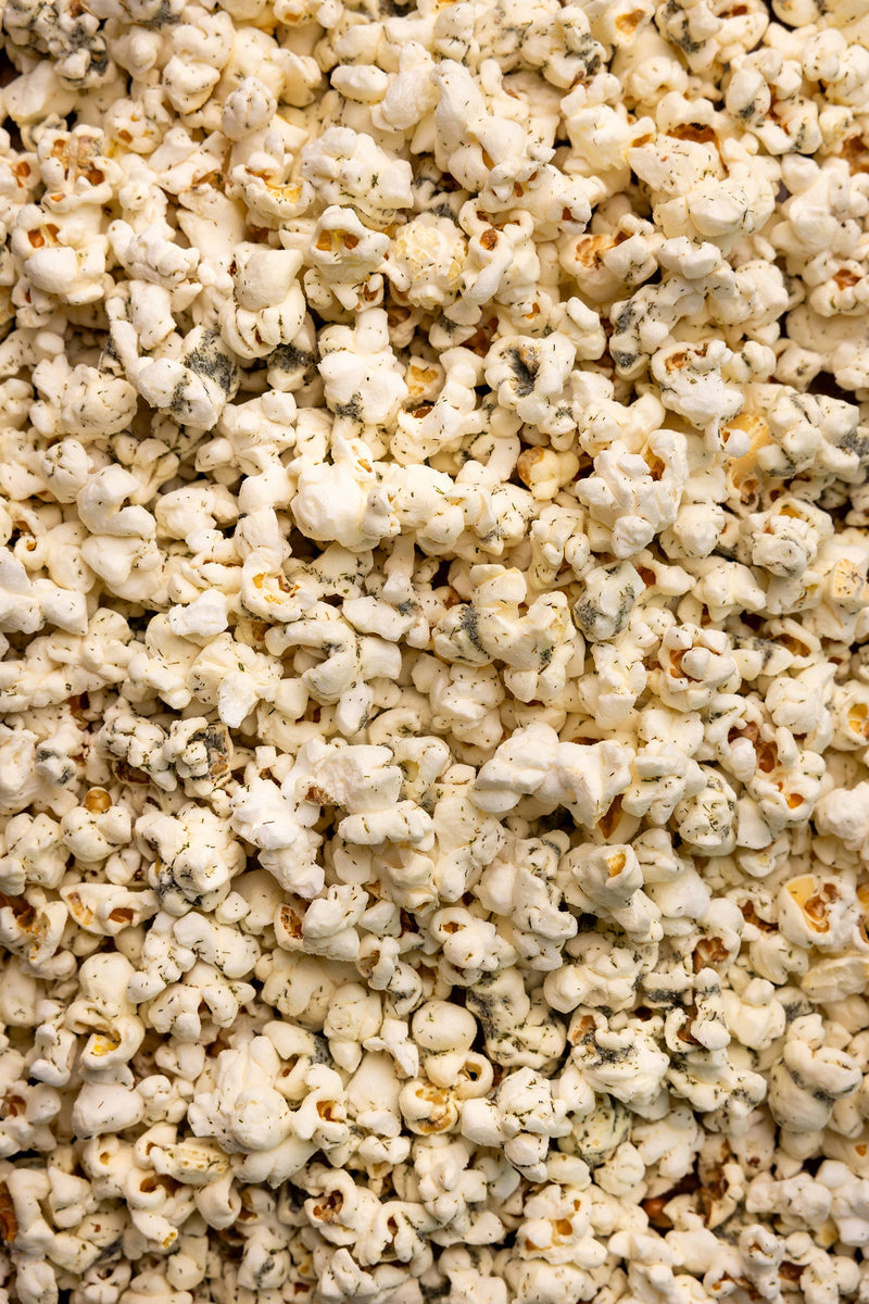 Poppy Hand-Crafted Popcorn - Dill Pickle Popcorn, a crunchy snack featuring white cheddar, vinegar, and dill, showcased in a pile. Perfect for culinary enthusiasts.