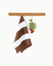 Striped Linen Tea Towel by MagicLinen, hanging on a wooden bar. Part of the zero-waste program, featuring a loop for easy kitchen hanging.