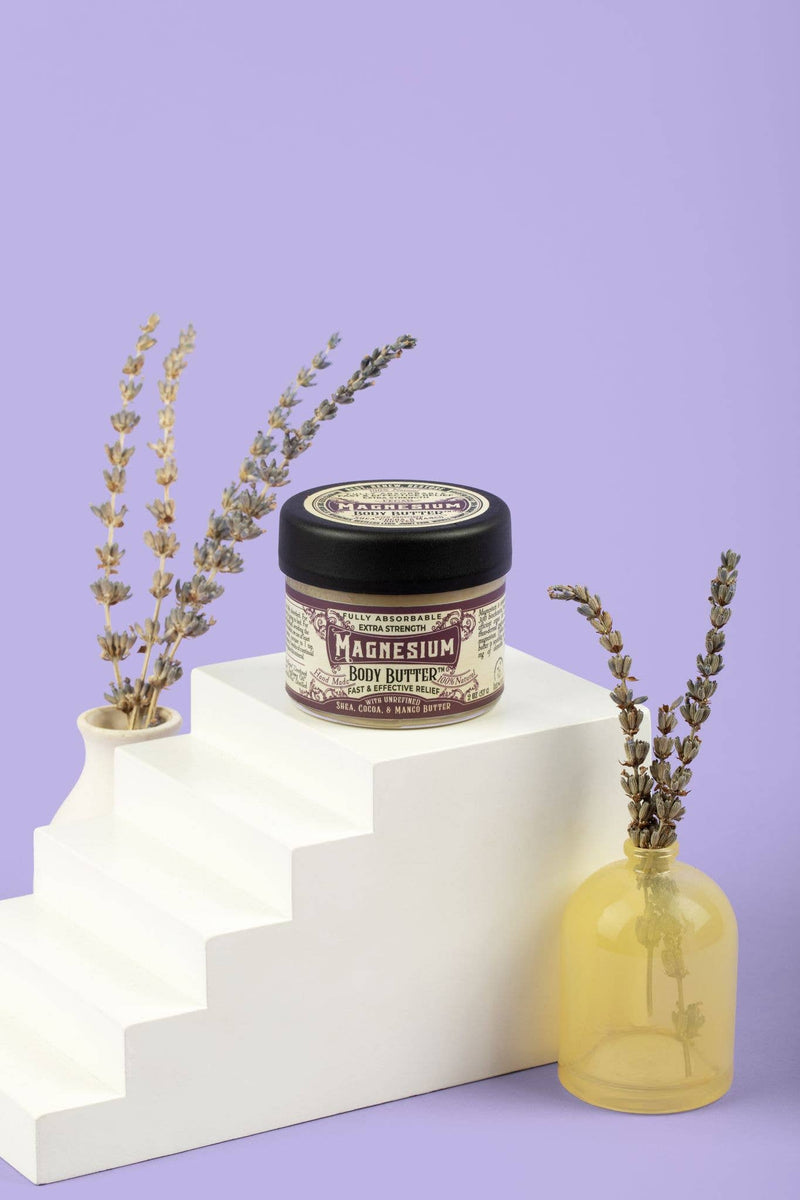Roots And Leaves - Magnesium Body Butter jar next to a vase of lavender, emphasizing its natural ingredients and soothing benefits for skin and muscle relief.