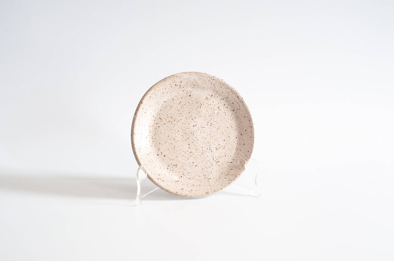 RachaelPots - Dessert Plate: Sage, a hand-thrown ceramic plate with a beige-brown speckled glaze, perfect for desserts, displayed upright on a clear stand.
