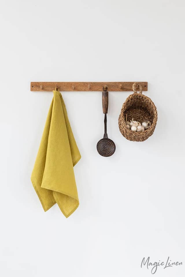 Linen tea towel with hanging loop on a rack, alongside a basket with garlic and onions, embodying MagicLinen's kitchen essentials.