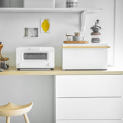 Yamazaki Home's Simple Steel Bread Box in White + Wood on a minimalist kitchen counter with a toaster-oven, coffee grinder, and decorative tray.