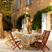 Couleur Nature - Forest Harvest Mustard & Blue tablecloth on a garden dining table, set for an outdoor meal with wooden chairs and sunlit stucco house backdrop.