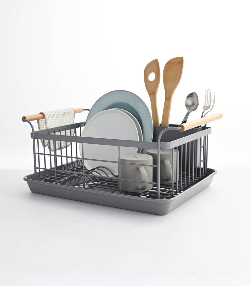 Yamazaki Home | Steel + Wood Dish Rack with Drainer Spout, featuring upright plate slots, utensil holder, and ash wood handles, showcased with kitchenware and a towel on the handle.