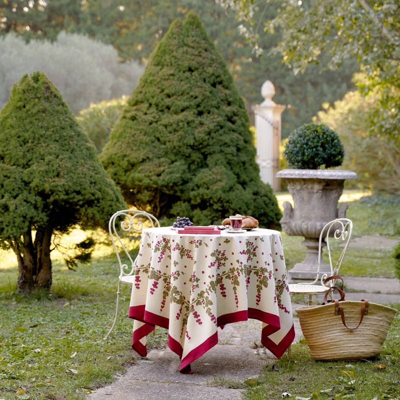 Couleur Nature - Gooseberry Red & Green tablecloth on a bistro table, set for breakfast with grapes, a croissant, coffee, and books, in a garden setting.