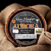 Nicola's Marketplace - DOP Aurora Manchego Kosher Cheese Wedge: 6 ounces, a whole wheel with branded rind, sits on burlap, showcasing its semi-firm texture.