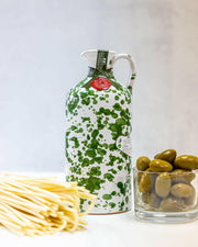 Frantoio Galantino Extra Virgin Olive Oil in a hand-painted ceramic jug, featuring green spots, alongside a glass of green olives and a red wax seal.