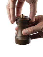 Close-up of the Peugeot | 1874 Manual Wooden Salt Mill Patinated, 4 inches, with hands adjusting the brass knob, showcasing its historical craftsmanship.