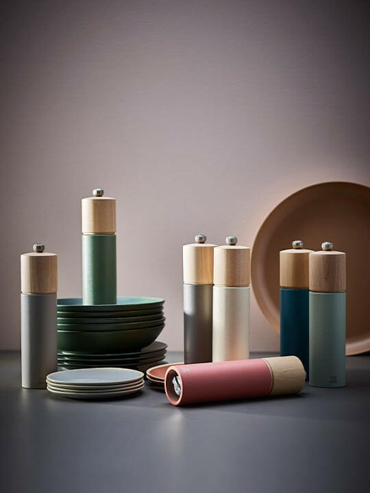 Peugeot Boreal Salt Mill in sage green, featuring a wooden top and adjustable metal knob, displayed with ceramic plates, exemplifying modern kitchenware elegance from Athens Cooks.