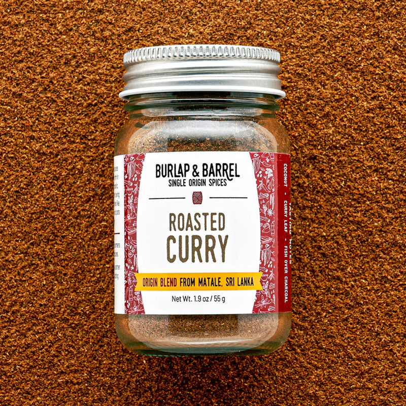 Burlap & Barrel | Roasted Curry spice blend in a glass jar, surrounded by loose curry powder. Ideal for enhancing hearty dishes with aromatic, roasted flavors.