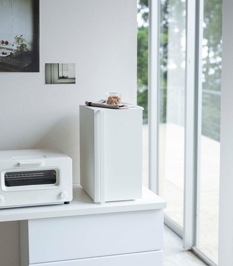 Yamazaki Home Bread Box, Vertical, Steel, Black sits elegantly in a minimalist kitchen nook, enhancing decor by reducing countertop clutter with its sleek design.