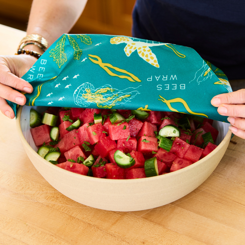 Bee's Wrap - Assorted 3 Pack - Oceans shown wrapping a bowl of watermelon and cucumber salad, illustrating reusable food storage use.