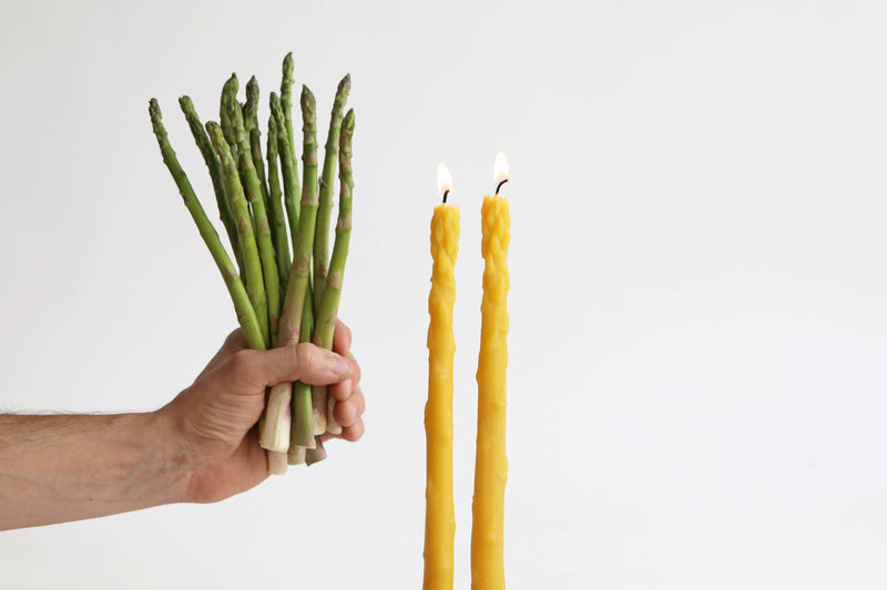 Artifaqt - Asparagus Beeswax Taper Candles (Pair): Green, resembling real asparagus, held next to a yellow candle, highlighting their unique design.