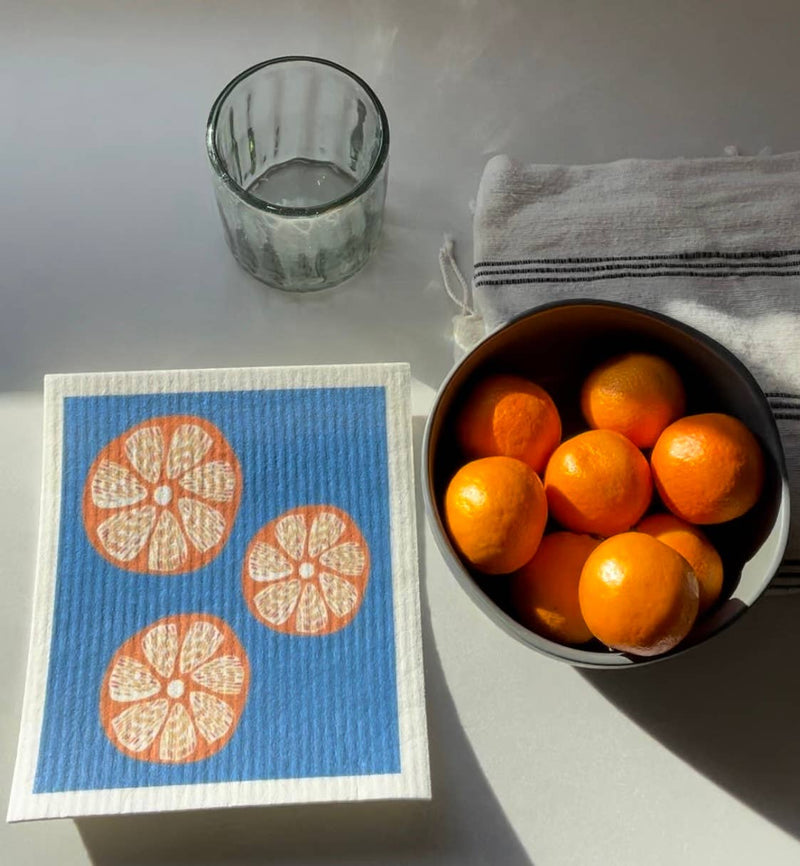 Ink and Fiber Designs - Oranges Swedish Dishcloth, depicted with a bowl of oranges, showcases its absorbency and eco-friendly features for versatile kitchen cleaning.