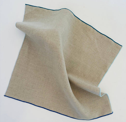 Tisch New York - Napkins in Natural Linen with blue hem, 18.5 square, displayed in soft folds, highlighting its pre-washed texture and contrasting edge.