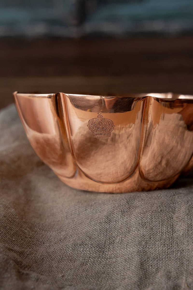 Coppermill Kitchen LLC - Vintage Inspired Copper Fluted Bowl with Crown Engraving, displayed on linen cloth, showcasing its elegant fluted design and embossed crown emblem.