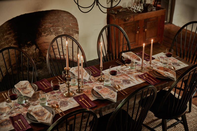Coral & Tusk - Autumn Blossoms Dinner Napkin elegantly folded atop dark stoneware plate, set in a rustic dining scene with brass candlesticks and gold flatware.