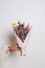 Idlewild Floral Co. - Bright Small Field Bouquet: a hand-tied arrangement of dried yellow, blue, and pink flowers, wrapped in pink paper with a cream ribbon.