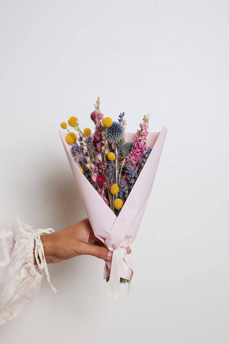 Idlewild Floral Co. - Bright Small Field Bouquet: a hand-tied arrangement of dried yellow, blue, and pink flowers, wrapped in pink paper with a cream ribbon.