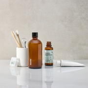 Davids Natural Toothpaste and Hydroxi™ fresh breath mouthwash with refill concentrate, bamboo toothbrushes, tongue scraper, and dental floss on a minimalist countertop.