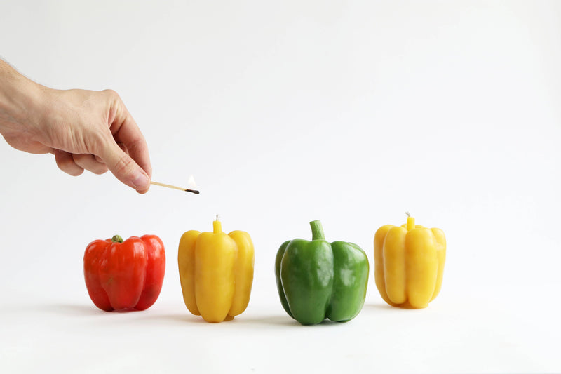 Artifaqt - Bell Pepper Beeswax Candle: Red, shaped like a red bell pepper, being lit with a match, showcasing its artisanal craftsmanship and natural beeswax composition.